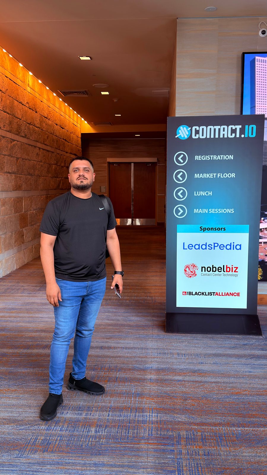 Wali Zuberi standing beside a Contact.io 2026 wayfinding sign at the conference in Denver, Colorado