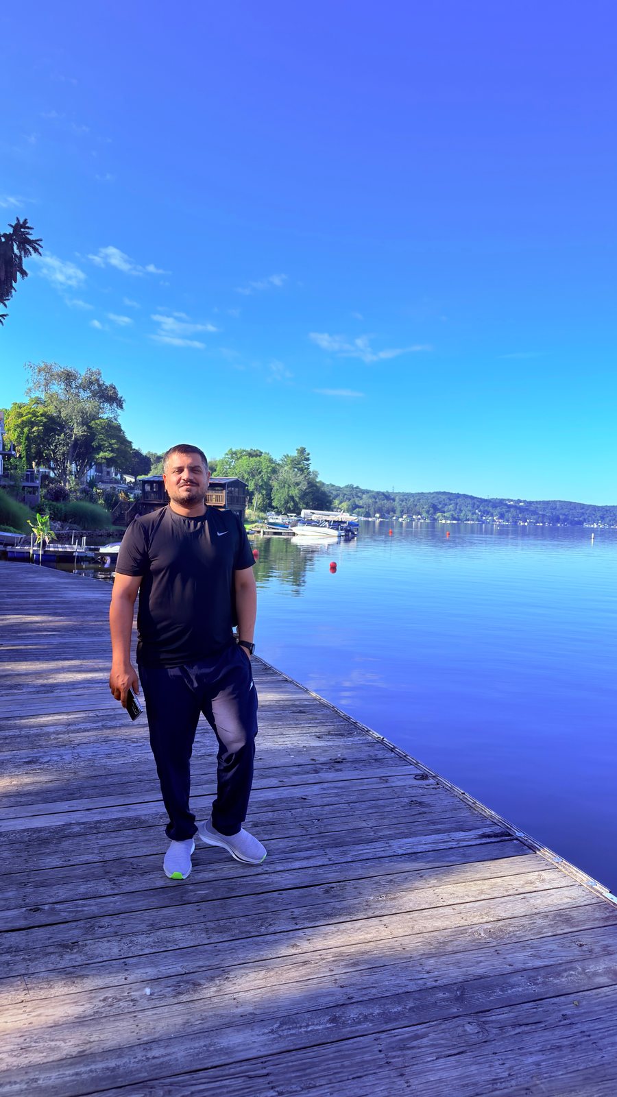 Wali Zuberi standing on a wooden lakeside dock on a sunny morning
