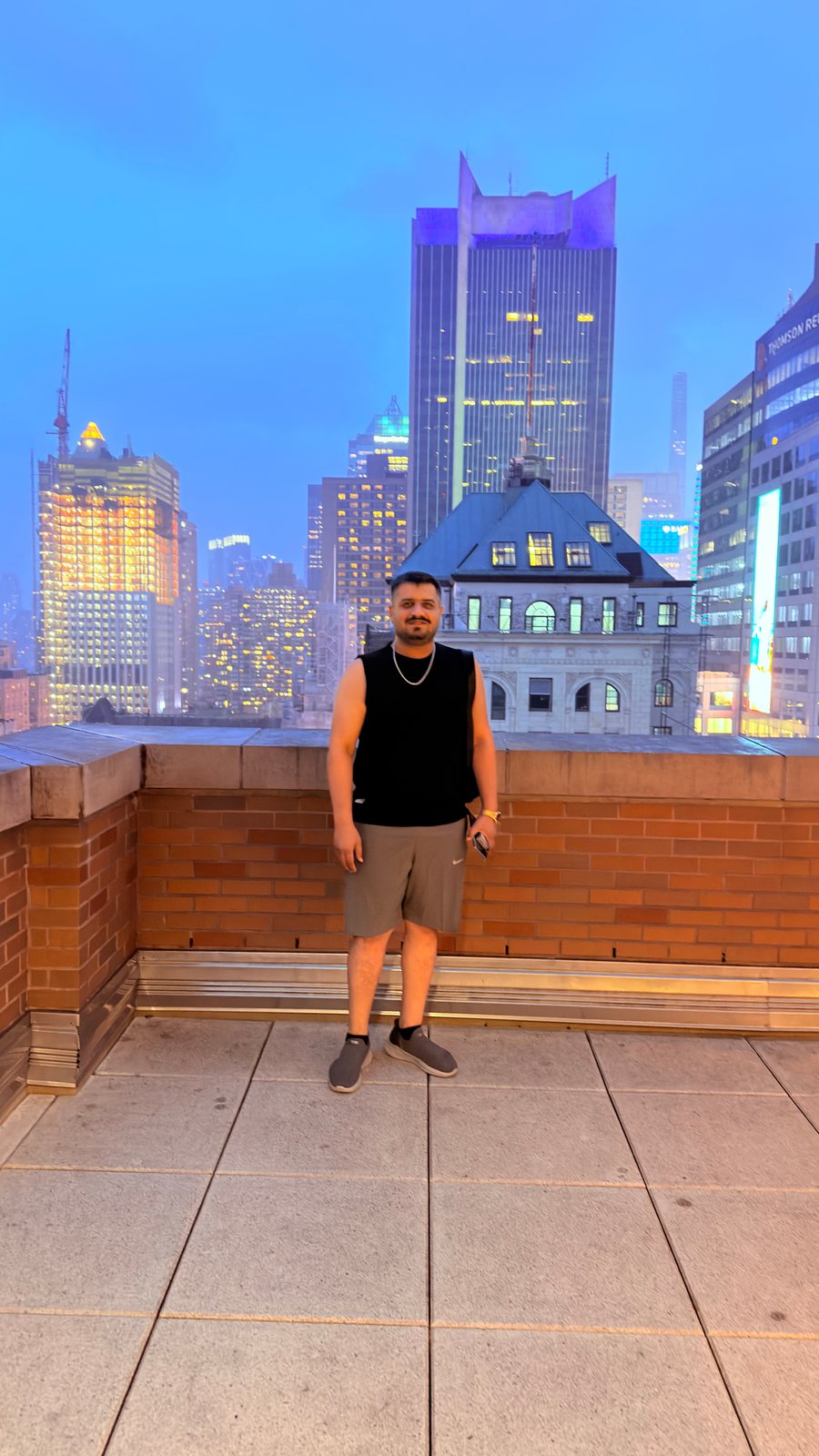 Wali Zuberi on a rooftop at dusk with the Midtown Manhattan skyline behind him